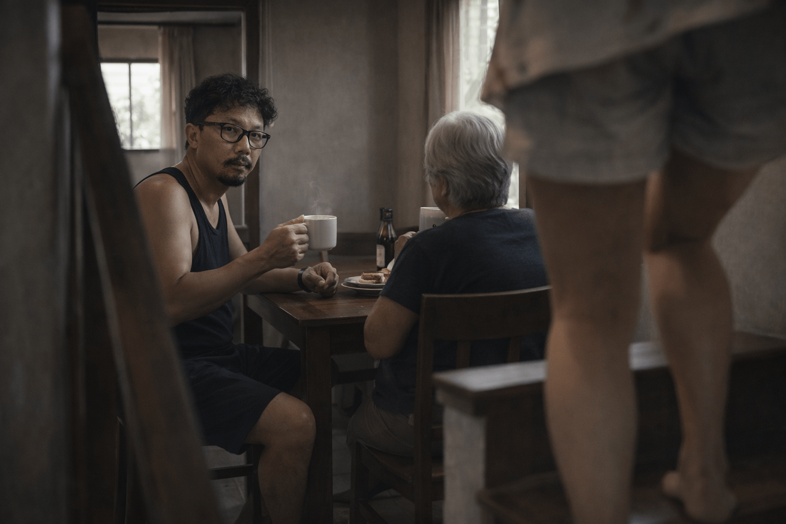 เช้าเงียบในบ้านเล็ก ผู้ชายถือแก้วกาแฟมองไปยังบันได ขณะที่หญิงชรานั่งหันหลัง และมีใครบางคนกำลังเดินลงมา